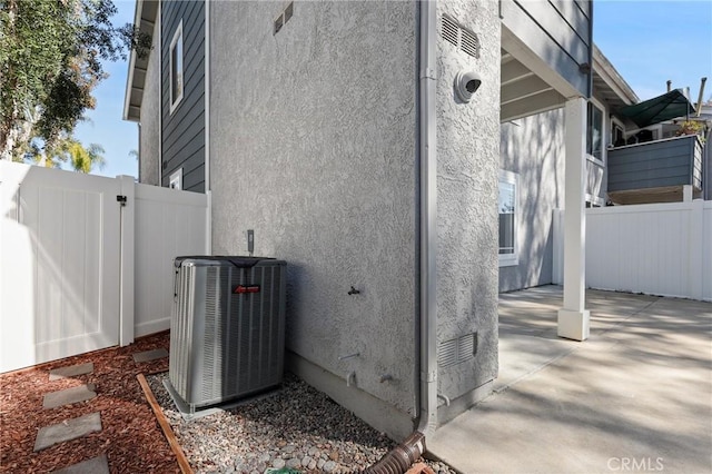 view of side of home with stucco siding, a patio area, central air condition unit, and fence