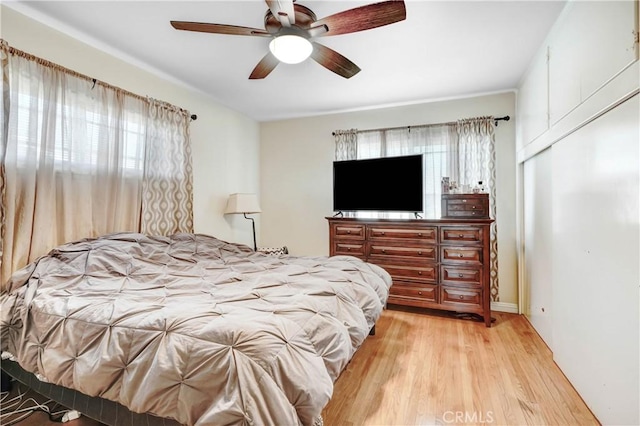 bedroom with a ceiling fan, multiple windows, light wood-style flooring, and a closet