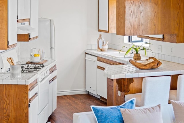 kitchen featuring a sink, white appliances, dark wood finished floors, baseboards, and under cabinet range hood