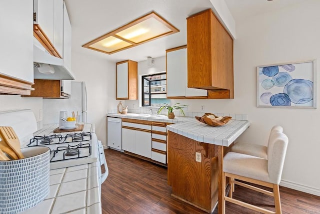 kitchen featuring white dishwasher, a breakfast bar, tile counters, range with gas stovetop, and dark wood-style floors