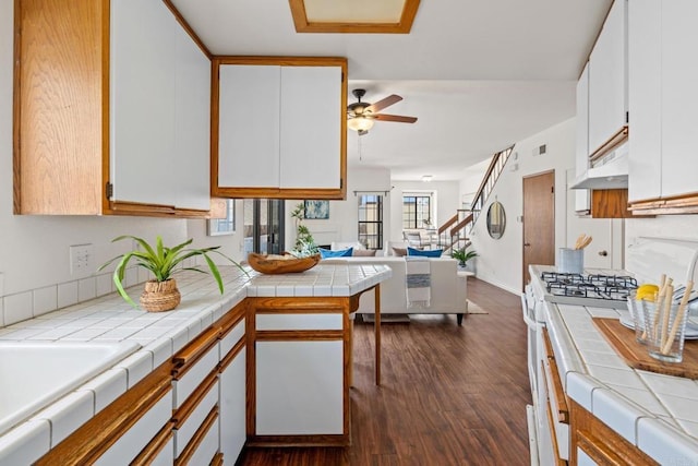 kitchen with tile counters, open floor plan, under cabinet range hood, and white cabinets