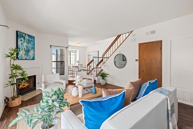 living area featuring visible vents, wood finished floors, baseboards, stairway, and a fireplace with flush hearth