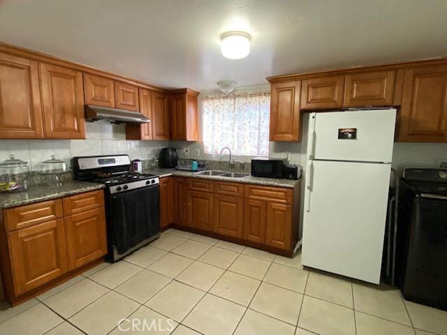 kitchen featuring washer / clothes dryer, gas range, brown cabinets, a sink, and freestanding refrigerator