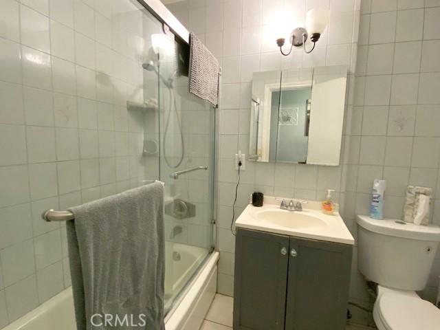 full bathroom with vanity, toilet, shower / bath combination with glass door, and tile walls