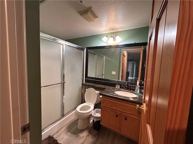 bathroom featuring vanity, wood finished floors, toilet, a textured ceiling, and a stall shower