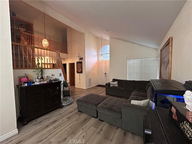 living area with baseboards, stairs, wood finished floors, and high vaulted ceiling