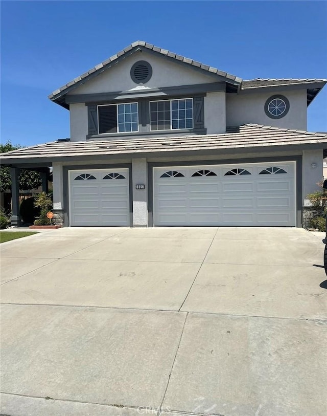 traditional home featuring stucco siding, a tiled roof, driveway, and a garage