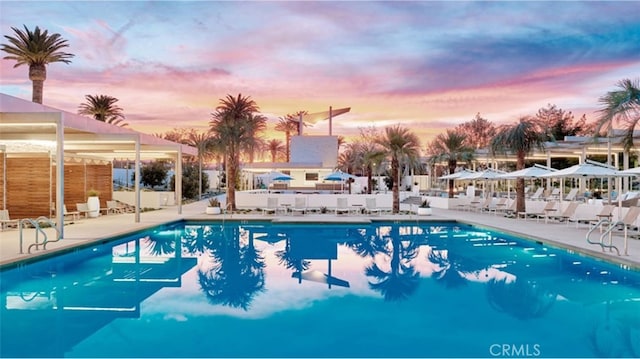 pool at dusk with a community pool, a patio area, and fence