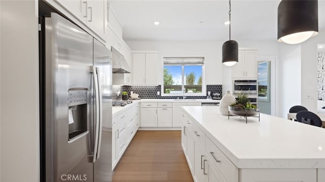 kitchen featuring appliances with stainless steel finishes, a sink, light wood-style flooring, backsplash, and under cabinet range hood