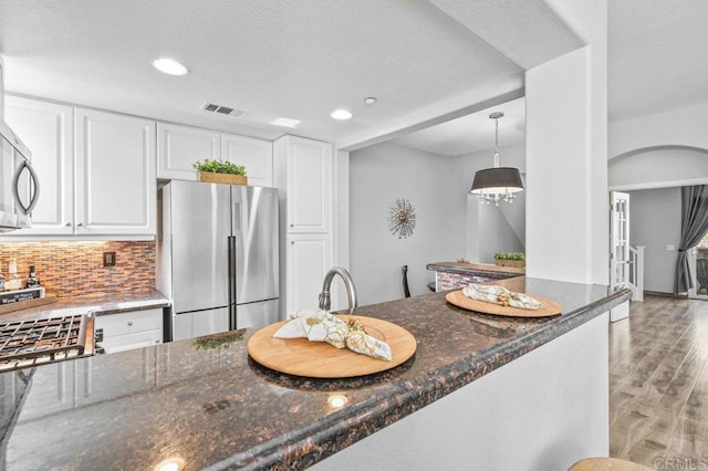 kitchen with light wood-type flooring, freestanding refrigerator, dark stone counters, and white cabinetry