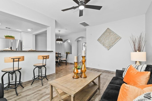 living area with light wood-style floors, arched walkways, ceiling fan, and visible vents