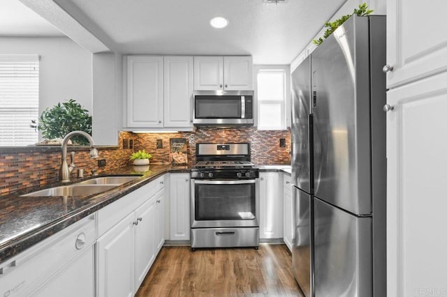 kitchen featuring white cabinets, dark wood-style flooring, a sink, stainless steel appliances, and decorative backsplash