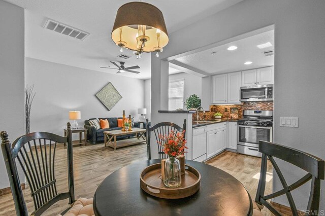 dining area with light wood-style floors, ceiling fan with notable chandelier, recessed lighting, and visible vents