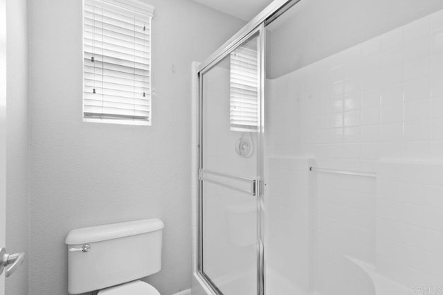 full bath featuring a shower with door and toilet