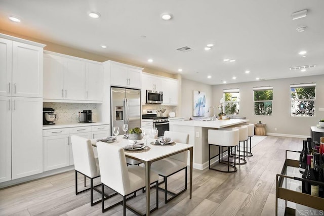 16755 Coyote Bush Dr Unit 32, San Diego, CA 92127 - kitchen with stainless steel appliances, an island with sink, light wood-style floors, a breakfast bar, and white cabinets