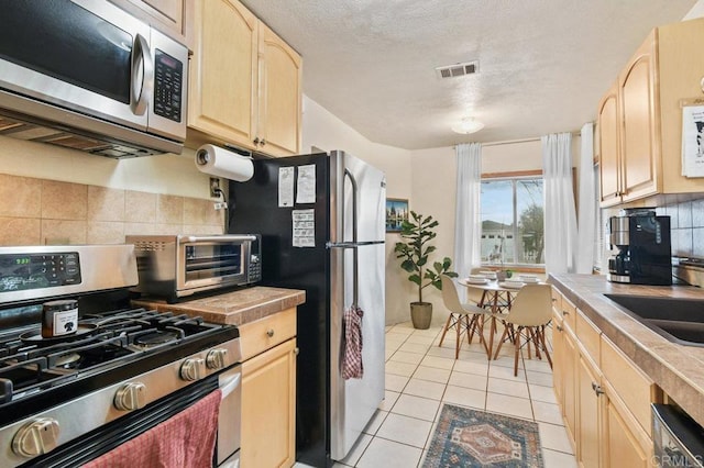 4580 60th St, San Diego, CA 92115 - kitchen with appliances with stainless steel finishes, light brown cabinets, decorative backsplash, light tile patterned flooring, and a textured ceiling