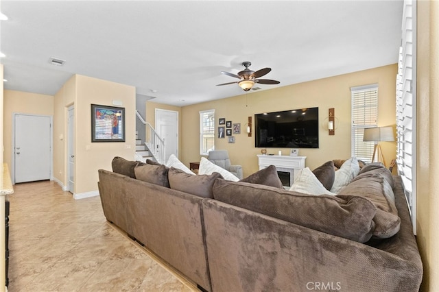 living area featuring stairs, a ceiling fan, and baseboards