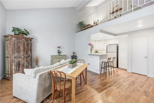 dining room featuring baseboards, light wood-style flooring, beam ceiling, and high vaulted ceiling