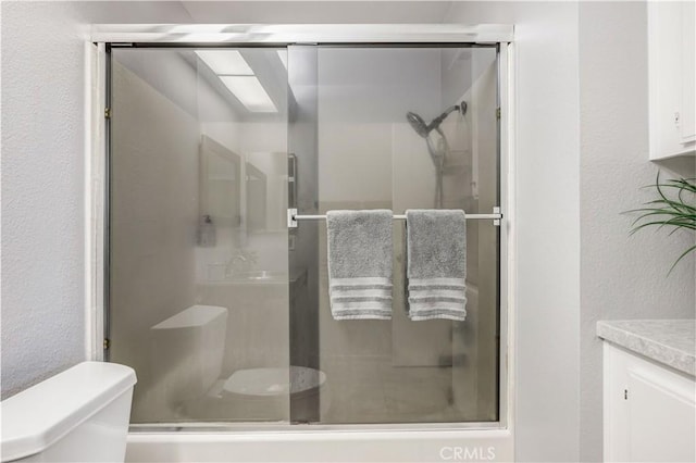 full bath with vanity, a textured wall, toilet, and a shower stall