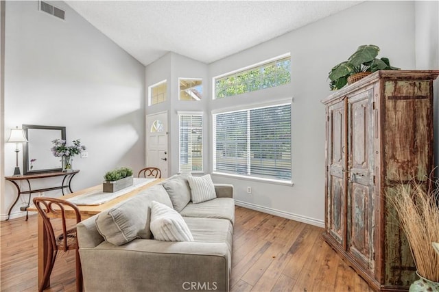 living area featuring high vaulted ceiling, visible vents, baseboards, and light wood finished floors