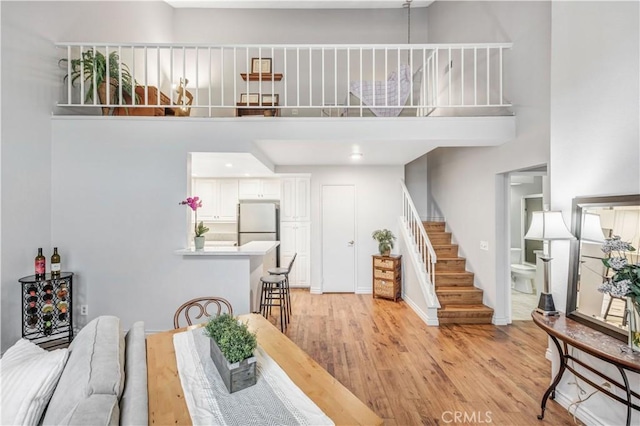 dining area featuring light wood-style floors, baseboards, stairs, and a towering ceiling