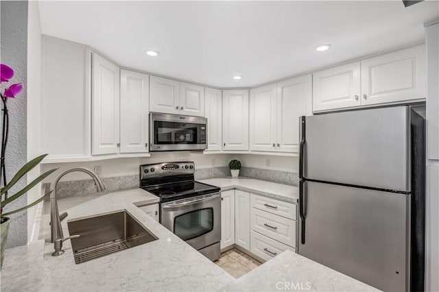 kitchen featuring light stone counters, a sink, stainless steel appliances, white cabinetry, and recessed lighting