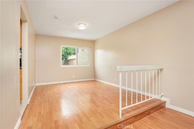 unfurnished room featuring baseboards, wood finished floors, and stairway