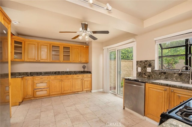 kitchen with tasteful backsplash, dishwasher, a sink, glass insert cabinets, and dark stone counters