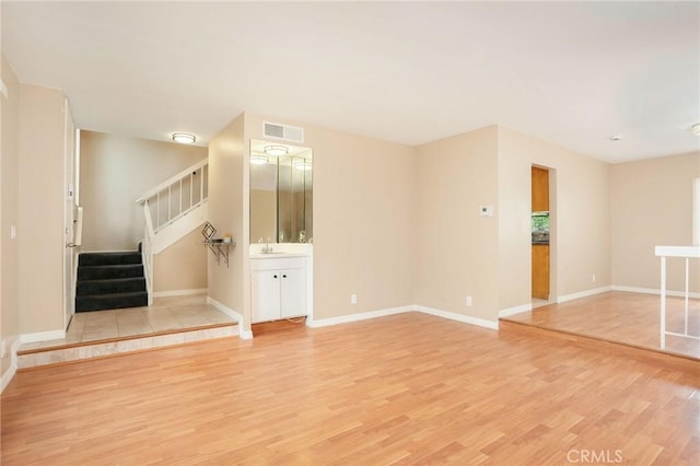 unfurnished living room featuring a sink, baseboards, light wood-type flooring, visible vents, and stairway
