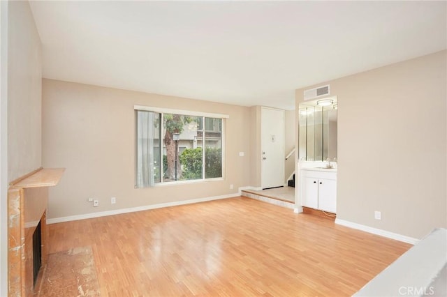interior space with visible vents, a fireplace, baseboards, stairs, and light wood-style flooring