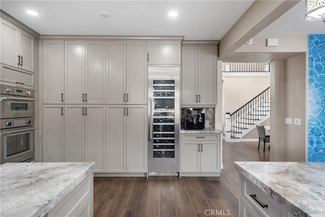 kitchen with dark wood-style flooring, stainless steel double oven, light stone counters, beverage cooler, and recessed lighting
