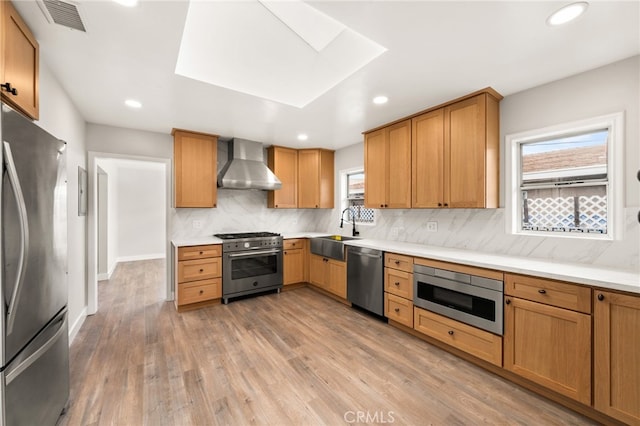 8392 Walker St, La Palma, CA 90623 - kitchen with stainless steel appliances, wall chimney exhaust hood, decorative backsplash, light wood-style floors, and a skylight