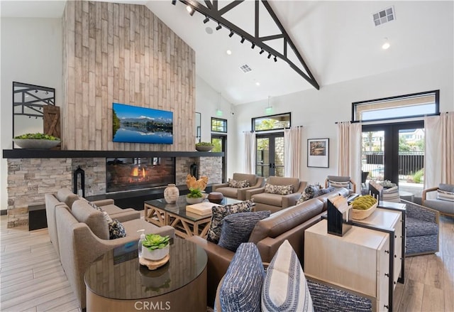 living room with visible vents, a glass covered fireplace, wood finished floors, and high vaulted ceiling