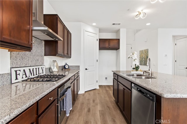 kitchen featuring visible vents, wall chimney exhaust hood, a sink, light wood-style flooring, and stainless steel appliances