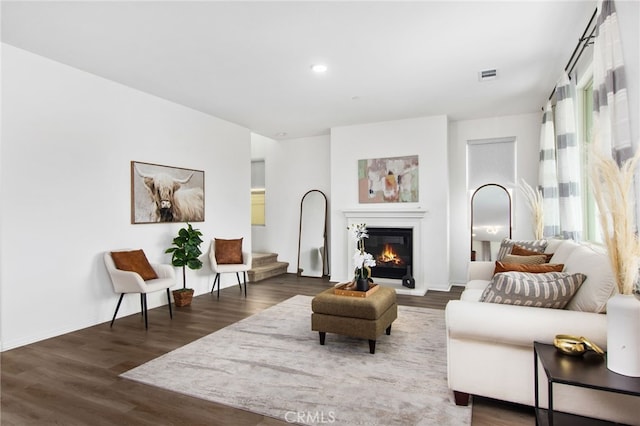 living room with a glass covered fireplace, baseboards, wood finished floors, and visible vents