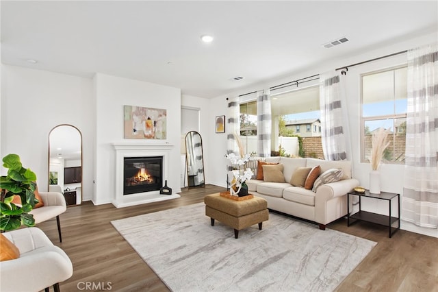 living area with a glass covered fireplace, recessed lighting, wood finished floors, and visible vents
