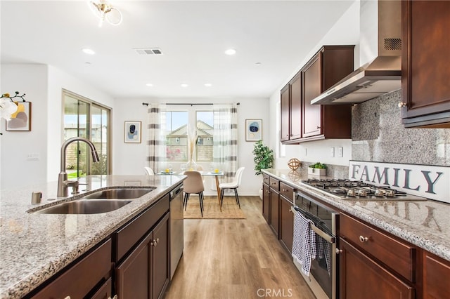 kitchen with wall chimney range hood, a sink, stainless steel appliances, light wood-type flooring, and visible vents