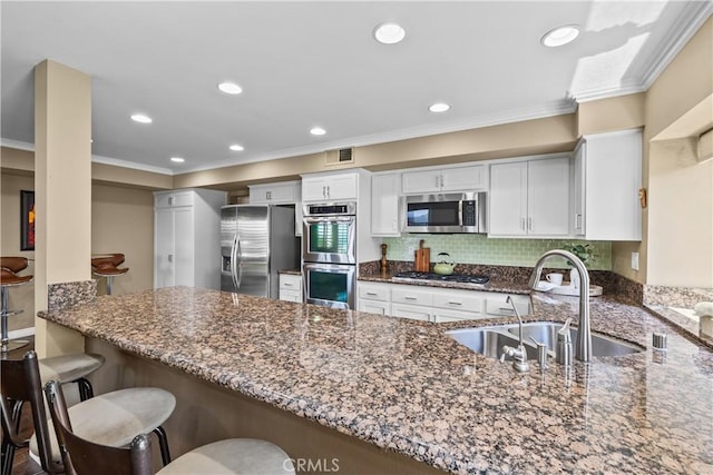 24239 Bella Ct, Newhall, CA 91321 - kitchen featuring appliances with stainless steel finishes, dark stone countertops, a peninsula, ornamental molding, and white cabinets