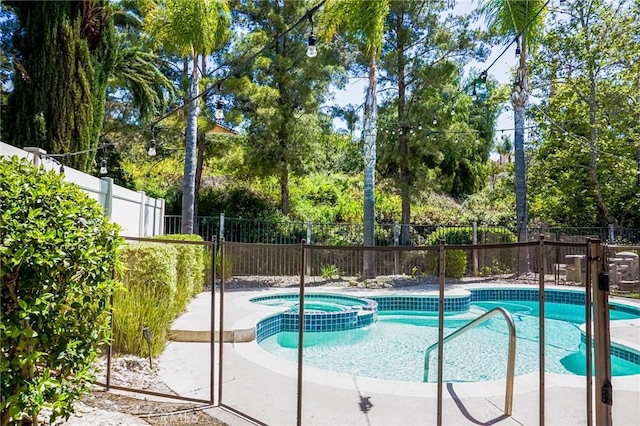 view of swimming pool featuring fence and a pool with connected hot tub