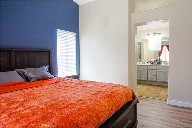 bedroom with lofted ceiling, ensuite bathroom, and light wood finished floors