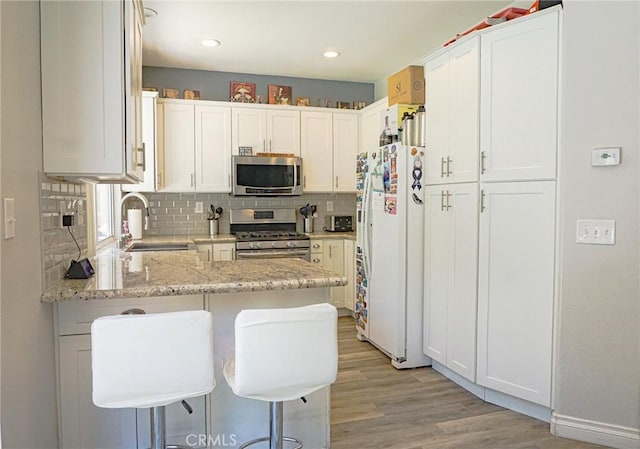 kitchen with decorative backsplash, appliances with stainless steel finishes, a sink, a peninsula, and light wood-style floors