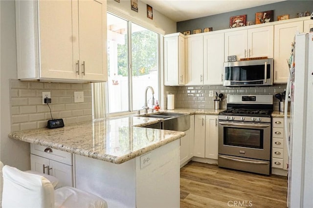 kitchen featuring appliances with stainless steel finishes, tasteful backsplash, a sink, white cabinets, and a peninsula