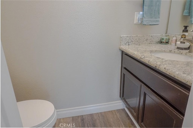 bathroom featuring baseboards, vanity, toilet, and wood finished floors