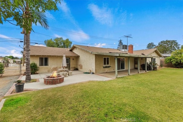 rear view of house with a lawn, a patio, stucco siding, and a fire pit