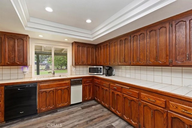 kitchen featuring tile countertops, dark wood-style flooring, a sink, stainless steel microwave, and black dishwasher