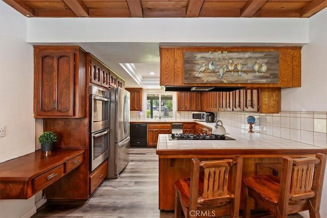 kitchen featuring tile counters, light wood-style flooring, a peninsula, beamed ceiling, and black appliances