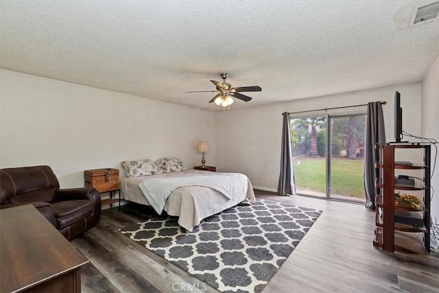 bedroom featuring access to outside, a textured ceiling, wood finished floors, and visible vents