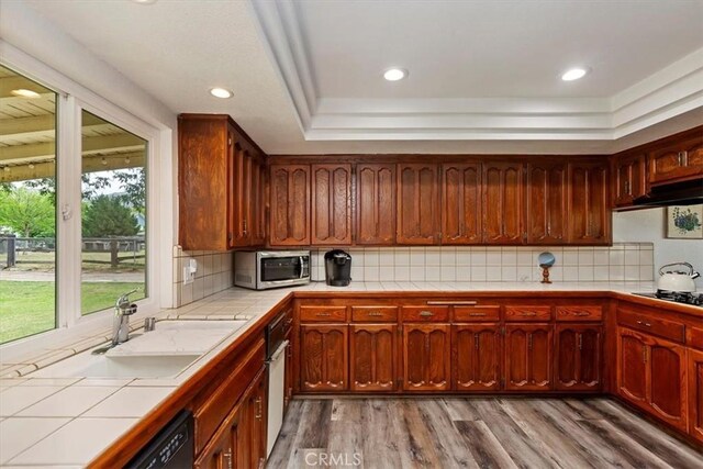 kitchen with a sink, light wood-style floors, tile counters, under cabinet range hood, and black appliances
