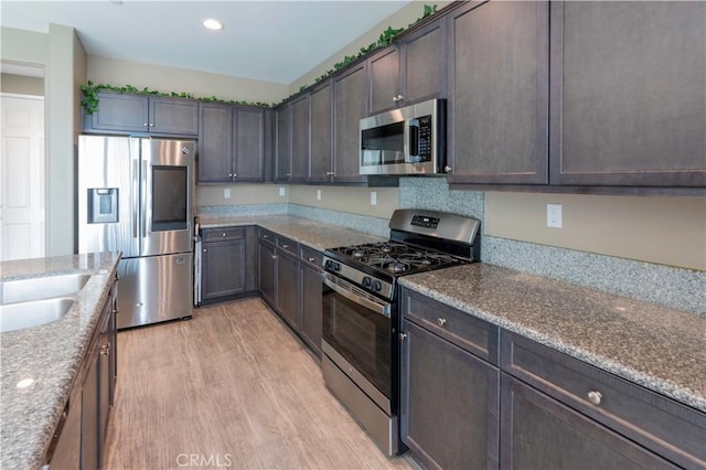kitchen featuring dark brown cabinets, stainless steel appliances, recessed lighting, stone counters, and light wood-type flooring