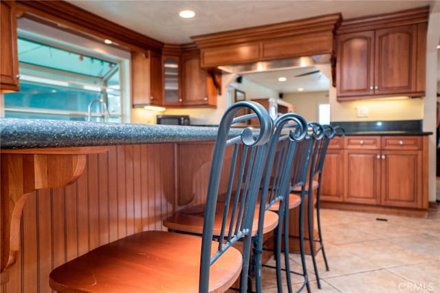 2136 Forbes Ave, Claremont, CA 91711 - kitchen with light tile patterned flooring, dark countertops, a breakfast bar, and brown cabinetry